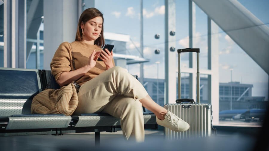 Young woman sitting in an airport departure lounge completes a survey on her smartphone.