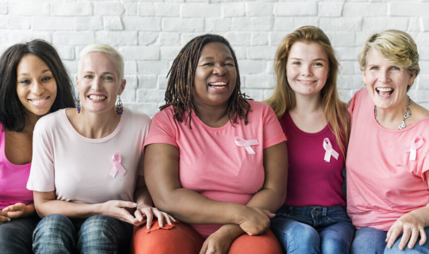 A group of breast cancer charity supporters sit smiling at the camera.