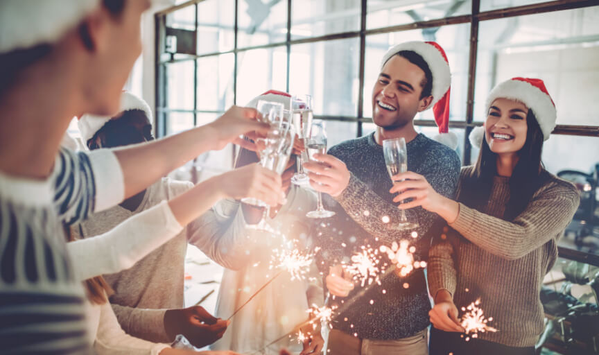 Employees enjoying an office Christmas party, holding sparklers and toasting with champagne flutes.