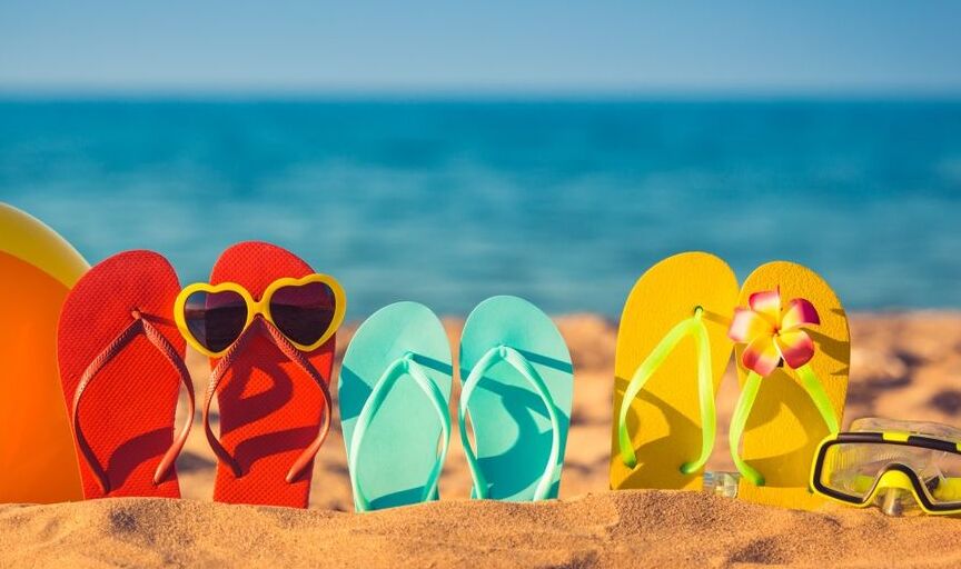 Colourful flip flops stuck into the sand on a sunny beach to illustrate holiday travel.